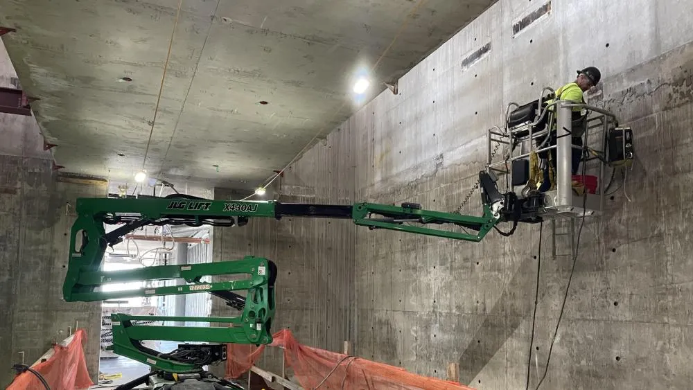 A May 2023 contest winner features a construction worker, hoisted by a green crane working on the interior of one of the buildings at Aggie Square. Photo by Jordan Levin.