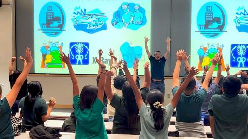 Students enthusiastically participate in a presentation about nursing, raising their hands above their heads.