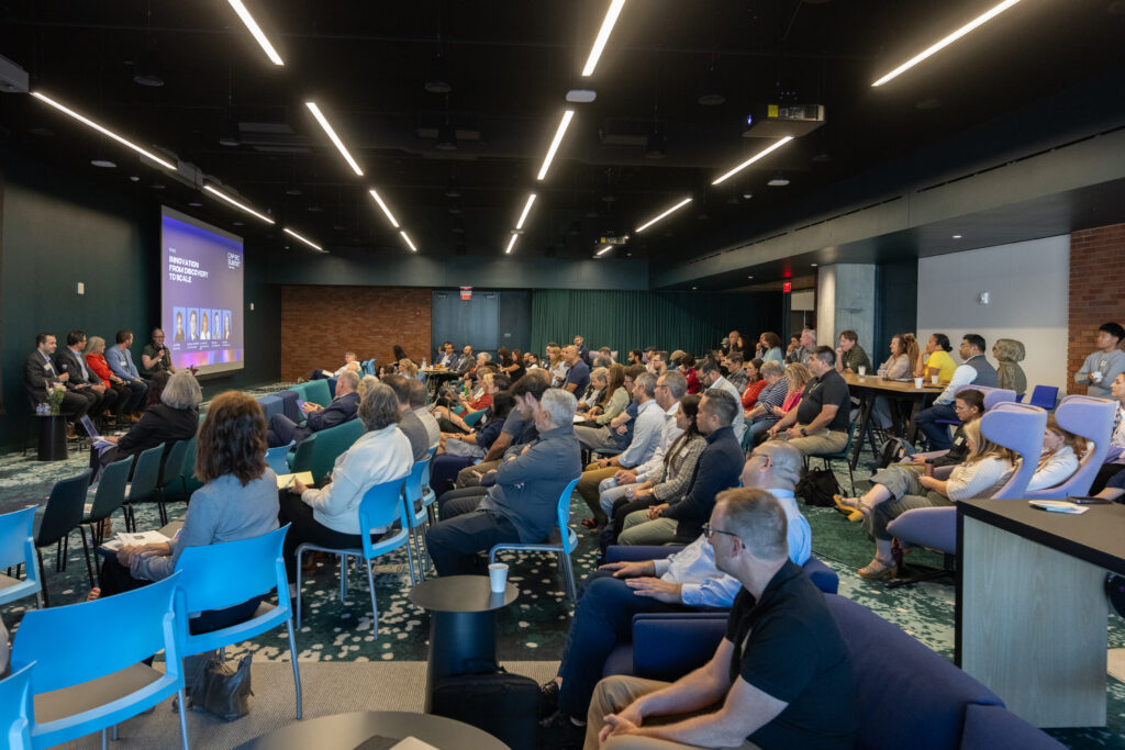 A room full of people sitting listening to a panel of speakers.